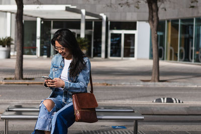 Full length of man using mobile phone while sitting on bench