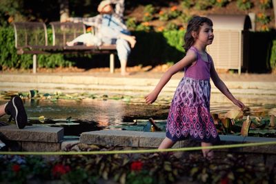 Side view of cute girl looking away while walking by pond in park