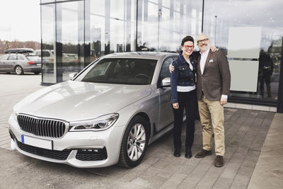 Portrait of senior couple standing by car against showroom