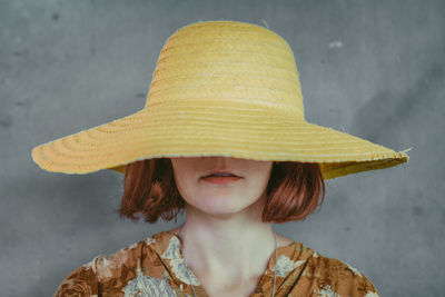 Close-up of young woman wearing yellow sun hat against wall