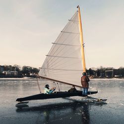 Three people in sailing canoe against sky