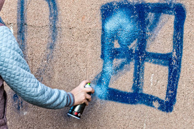 Cropped hand of person painting with spray on wall