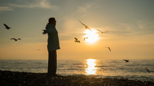 Silhouette woman standing at beach against sky during sunset