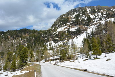 Road amidst trees and snowcapped mountains against sky