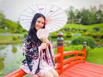 Portrait of smiling young woman sitting on railing at footbridge