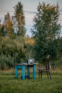 Empty chairs and table on field against trees