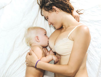 Mother feeding breast to daughter on bed