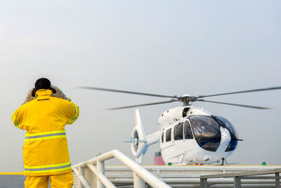 Rear view of worker standing against helicopter