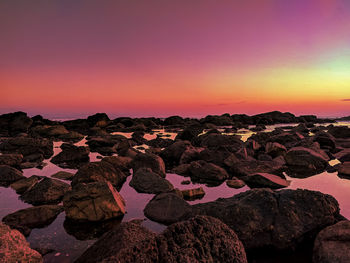 Rocks by sea against romantic sky at sunset
