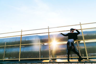 Low angle view of woman walking on chainlink fence against sky
