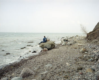 Rear view of friends sitting on rock at beach