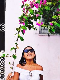 Portrait of smiling young woman wearing sunglasses standing against plants