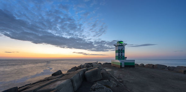 Lighthouse by sea against sky during sunset