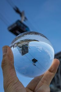 Close-up of hand holding crystal ball against blue sky