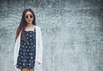 Portrait of a young woman wearing sunglasses standing against wall