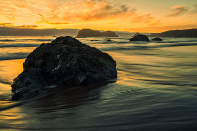 Rock formation in sea against sky during sunset