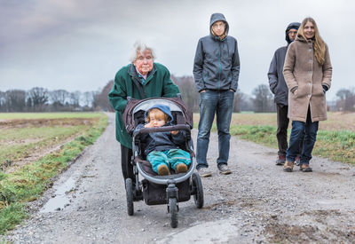 Family with baby walking on dirt road against sky during winter