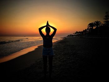 Rear view of couple standing on beach at sunset