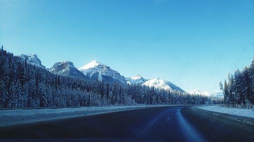 Road by snowcapped mountains against sky during winter