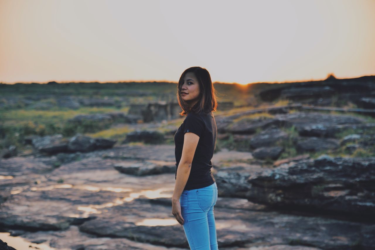 one person, standing, sky, young adult, real people, lifestyles, leisure activity, sunset, young women, looking at camera, women, nature, focus on foreground, adult, casual clothing, three quarter length, portrait, land, side view, outdoors, beautiful woman, hairstyle