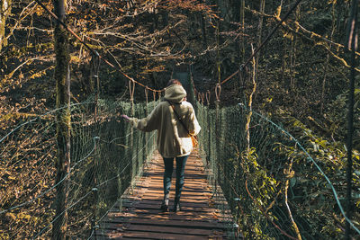 Rear view of man walking on footbridge in forest