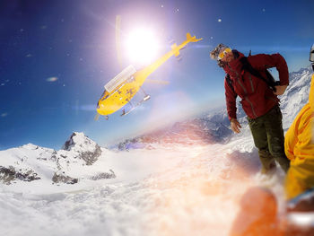 Young man standing on snow covered field against sky with helicopter