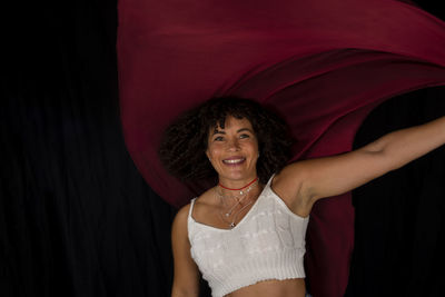 Woman moving a red cloth over her head against a black background. happy woman. salvador, brazil.