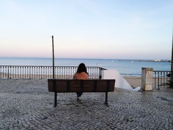 Rear view of woman relaxing on beach at beach against clear sky during sunset