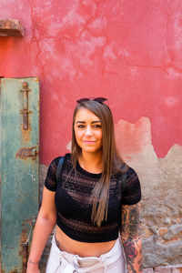 Portrait of smiling young woman standing against wall