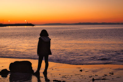 Rear view of woman standing on beach during sunset