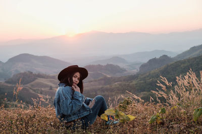 Woman sitting on mountain against sky during sunset