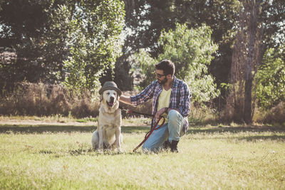 Mid adult man with dog wearing hat on grassy field