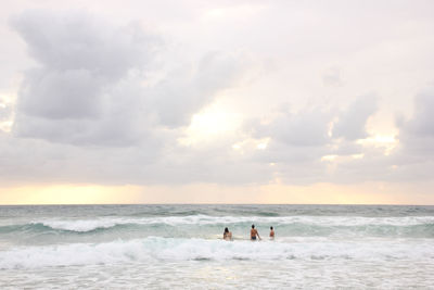 People in sea against sky during sunset