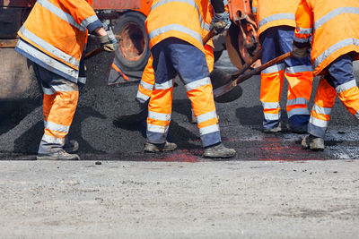 A road worker is spreading fresh asphalt with shovels over the repair area to repair section of road
