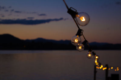 Row of illuminated light bulbs over river against sky