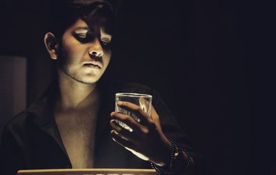 Close-up of young man holding sunglasses against black background