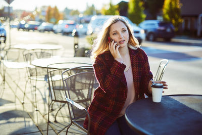 Young woman talking on mobile phone while sitting at sidewalk cafe