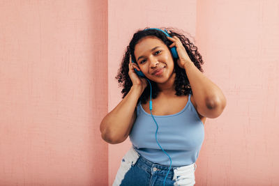 Portrait of young woman listening music standing against wall