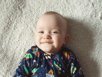 High angle portrait of cute smiling baby boy lying on bed at home