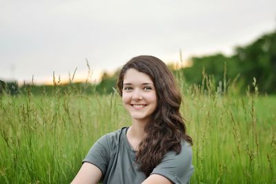 Portrait of smiling young woman on field against sky