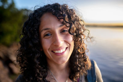 Mixed-race woman looking at camera and smiling while enjoying outdoors at sunset.