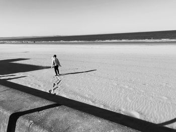 Girl walking on wet sand against clear sky