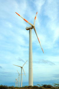 Low angle view of windmills against cloudy sky