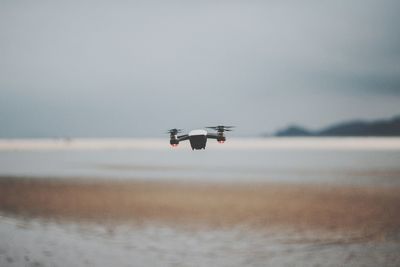 Drone flying over sea against sky