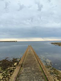 Pier on sea against cloudy sky