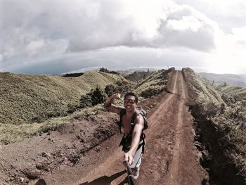 Happy hiker with monopod showing bicep on dirt road against sky