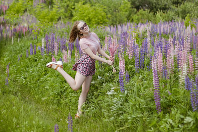 Young woman in the field of flowers with bunch of lupines dancing