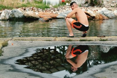 Side view of shirtless man sitting on rock by lake