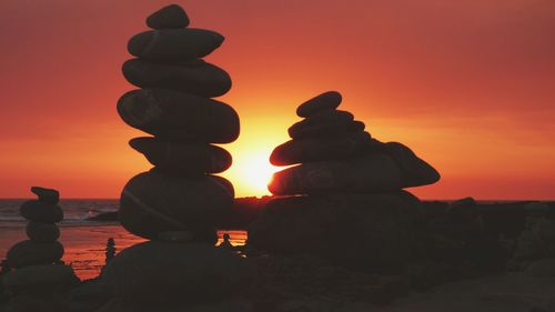 Stack of rocks on sea against sky during sunset