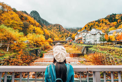 Rear view of woman by railing looking at stream against sky